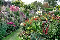 Packed flower beds, in foreground hot theme of red, yellow and purple flowers whilst beyond a bed of pink and purple flowers