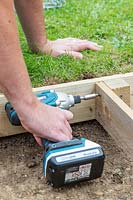 Man fixing a wooden board to corner post using an electric screwdriver