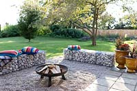 Finished firepit area with colourful cushions on gabion benches and pebble surface