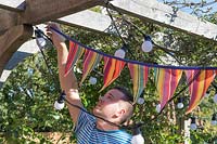 Man hanging up colourful bunting on underside of pergola