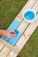 Man using a paintbrush to paint the wood before assembling the picnic bench