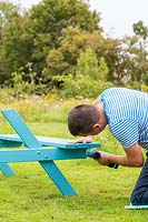 Man using an electric screwdriver to fix seat to bench