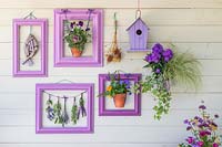 Purple themed wall display including painted birdhouse, driftwood fish, pots of Violas and bunches of drying flowers