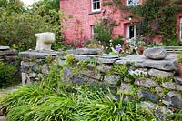 Stone wall in front of pretty pink Welsh cottage with decorative pebble and contemporary sculpture. 