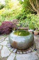Decorative raised pond amongst colourful summer Acer foliage on shaded patio with seat