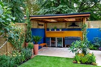 Patio and outdoor room with covered barbecue, surrounded by a contemporary wooden slatted fence and blue painted wall