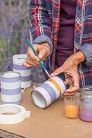Woman using a small paint brush to add orange stripe to tin cans