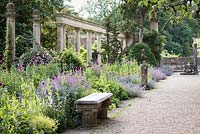 A border full of Papaver - Opium Poppy -  and Nepeta - Catmint - backed by a colonnade and surrounded by sculptural fragments 