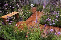 A path of wooden boards surrounded by colourful perennials leading to a contemporary Carrara marble sculpture. 'A Place to Think' garden by Southend Young Offenders'. 