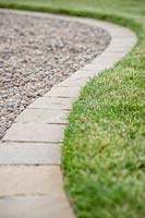Path edge made from square pavers, edging between lawn and gravel path. 