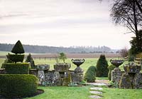 Pair of classic urns displayed on stone wall in the Topiary garden, with views out to surrounding fields at Rodmarton Manor, Glos, UK. 