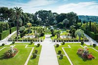 View of the main parterre, or French garden, designed to look like the deck of an ocean liner, ship. Features include manicured lawns, clipped topiary, palms including Butia capitata and Phoenix canariensis, and a water garden with fountains which play intermittently, synchronised to music. A classical gazebo forms a focal point at the far end. Villa Ephrussi de Rothschild.
