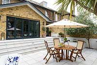 Wooden dining furniture with umbrella and a view to house with steps up to bifold doors