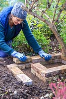 Woman adding second layer of bricks to the hedgehog house walls