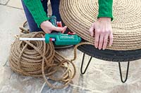 Woman using glue gun to cover tyre table with jute rope