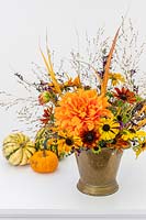 Autumnal arrangement including Rudbeckia, Helenium, Dahlia, Salvia and ornamental grasses in brass vase.