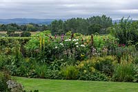 Border planted with dahlias and herbaceous perennials including linaria, helianthus, verbascum and phlox. Beyond, glimpses of Blackmore Vale.