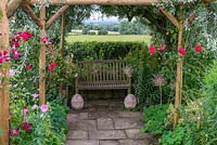 View along a path beneath a rustic pergola to a bench, with views over Blackmore Vale beyond.
