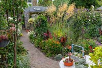 A curving path leads from dining table to shed, passing a central bed planted with Stipa gigantea, Verbena bonariensis, hydrangeas, heleniums, alliums, cannas, roses, dahlias, dierama and penstemon.