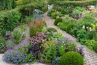 A bird's eye view of a contemporary garden design, a diagonal brick path separates a gravel garden from beds of perennials and grasses, interspersed with Taxus - Yew - ball topiary 