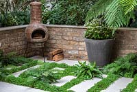 Porcelain tiles interplanted with ferns and Soleirolia soleirolii - Mind-your-own-business. Pot of white begonias and chiminea in front of raised beds