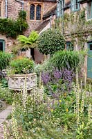 Courtyard gravel garden with large ornate natural stone urn and planting which includes Verbascums, Nigella damascena -love-in-a-mist, and Salvias. 
