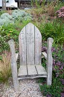 Engraved decorative wooden child's seat amongst late summer planting. Sedlescombe Primary School, Sussex, UK. 