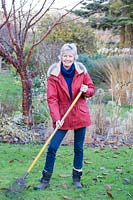 Woman standing with rake on lawn in front of a mixed bed