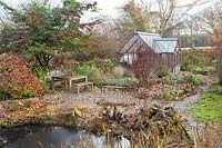 View over pond to garden seating with greenhouse beyond