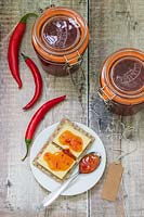 Chilli jam in kilner jar, chillies and plate of crackers and cheese. 