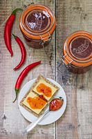 Chilli jam in kilner jar, chillies and plate of crackers and cheese. 