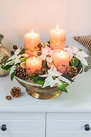 An arrangement in a golden bowl, with four coral pillar candles, Poinsettia flowers and cones 