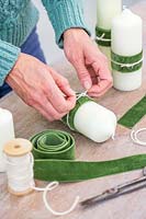 Woman adding a decorative velter green ribbon and cream string to the pillar candle