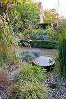 Water feature in gravel garden with ornamental grasses Festuca glauca, Miscanthus sinensis, Molinia and Carex.