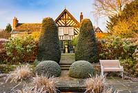 View of the house from the Lower Rill Garden on a frosty December morning. Planting includes: Iris ensata, clipped yew trees, balls and hedge 'Taxus baccata' a beech hedge 'Fagus' and Hydrangea macrophylla.