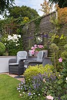 Grey rattan chairs in front of grey painted wall by lawn in cottage garden