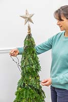 Woman decorating space saving christmas tree with LED fairy lights