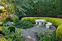 Tiered curved hedges around a circular paved area with stone furniture 
