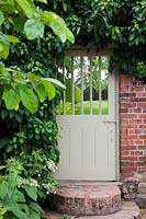 Painted wooden gate in walled garden with climbing  Hydrangea petiolaris.