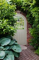 Painted wooden gate in walled garden with climbing Hydrangea petiolaris and Hostas. 
