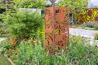 A corten steel rusted sculpture on a mixed flower border. The Sunken Retreat. RHS Malvern Spring Festival, 2016. Design: Ann Walker for Graduate Gardeners