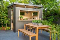 Metal outdoor kitchen bar on porcelain stone patio with wooden bench and table with Mentha - Mint in zinc containers. B and Q Bursting Busy Lizzie Garden 