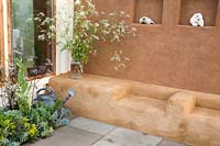 Cob and clay plastered wall with shelves and seating area small patio - border planted with herbs, kale and a glass vase with cow parsley. An Artist's Studio Home - Green Living Spaces. RHS Malvern Spring Festival May 2019 -  Design: Jessica Makins 
