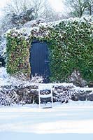 Snow-covered chair by garage with ivy. Veddw House Garden