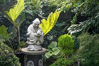 Standing figure mounted on pedestal surrounded with greenery