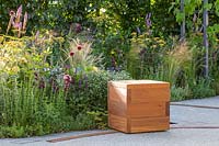 Moveable wooden cube seating on a rail with resin bound pathway in front of mixed summer border. The Crest Nicholson Livewell Garden - Hampton Court Flower Show 2019 