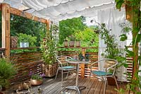 Summer balcony with seating, surrounded by vegetables planted in pots and greenery.