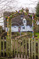 Christmas fairy lights over rose arches in December, over path leading to a thatched cottage.
