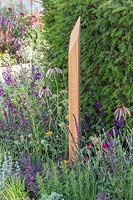 Wooden post with inscription in colourful bed with perennials in front of Taxus baccata hedging. The Cancer Research UK Pledge Pathway to Progress - Hampton Court Flower Festival, 2019.