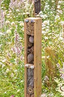 Vertical insect hotel towers in wildlife garden surrounded by wildflowers. Springwatch Garden, Hampton Court Flower Show, 2019.